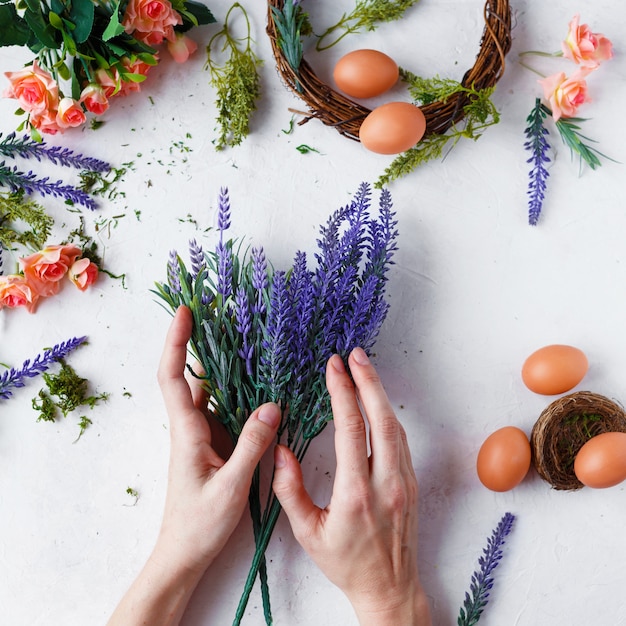 Frauenhänden machen Ostern Kranz aus Blumen, Kräutern und Eiern auf grau