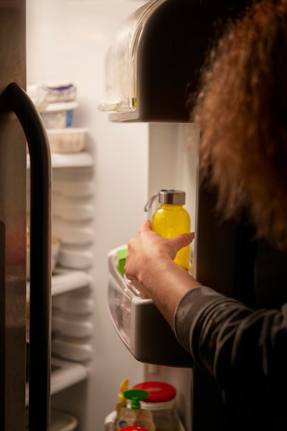 Frauenhand am offenen Kühlschrank nachts ausgestreckt zu einer Flasche Getränk