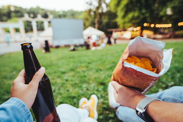 Frauenhand, die Bierflasche hält Mannhand, die Chips Open-Air-Kino hält