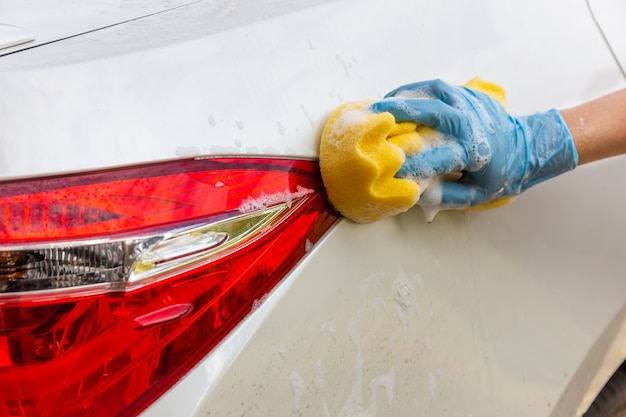 Frauenhand, die blaue Handschuhe mit waschendem modernem Auto des Rücklichts des gelben Schwammes trägt