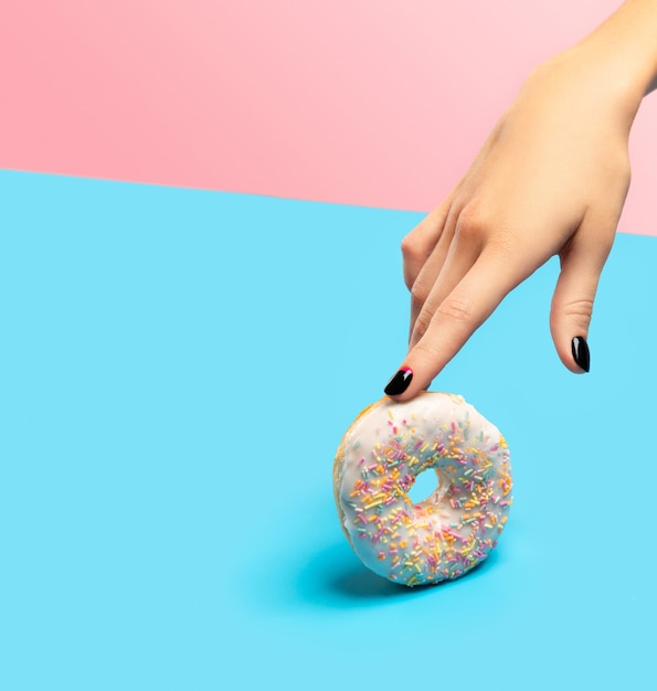 Frauenhand, die bunten Donut über blaue Oberfläche hält
