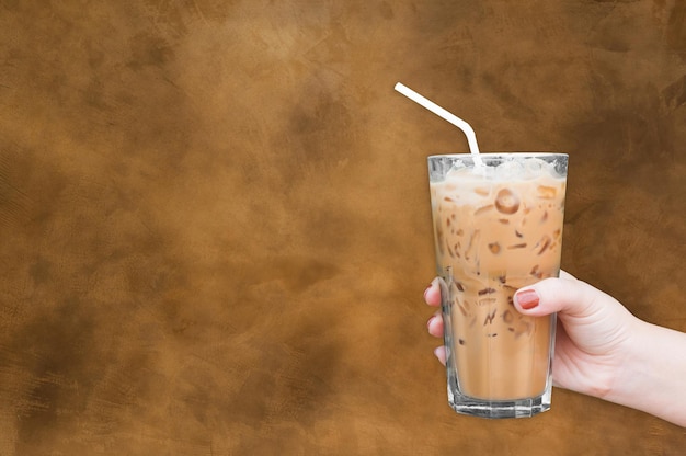 Frauenhand, die den Glaseiskaffee auf braunem grungy Wandhintergrund hält