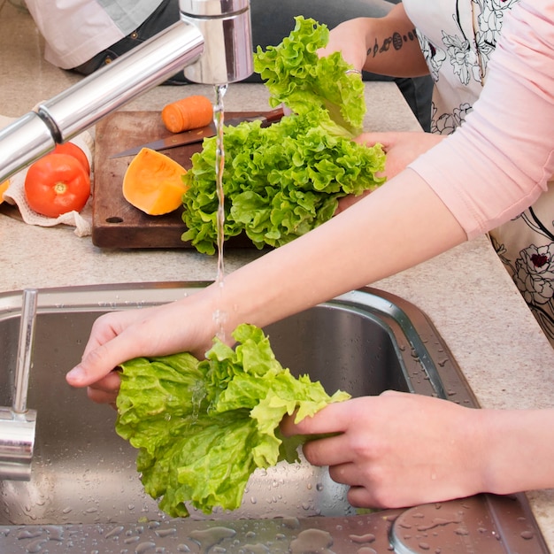 Foto frauenhand, die den kopfsalat im spülbecken wäscht