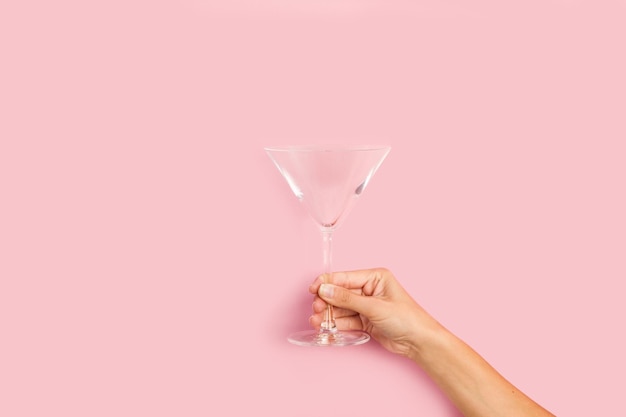 Frauenhand, die ein Cocktailglas auf einem rosa Hintergrund mit Kopienraum hält