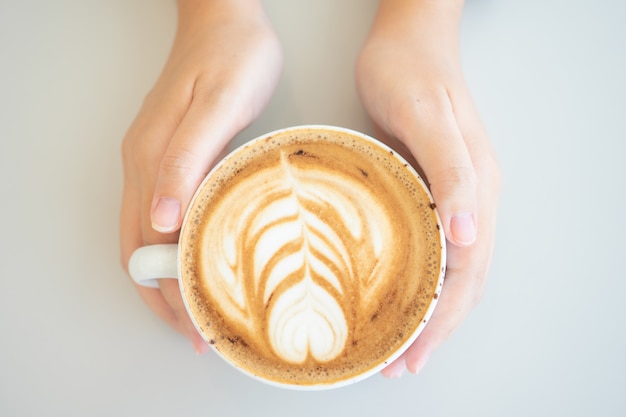 Frauenhand, die eine weiße Kaffeetasse hält. Kaffee ist eine Latte.