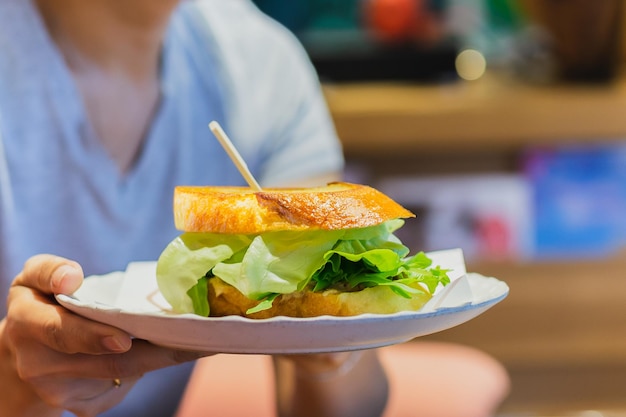 Frauenhand, die Gemüsesandwich auf einem weißen Teller im Café hält