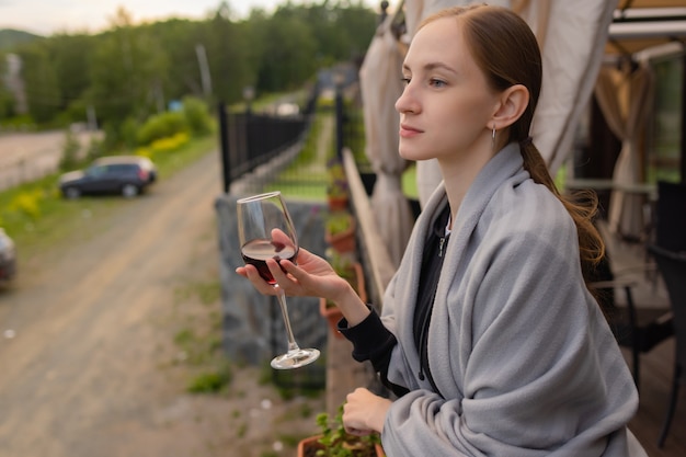 Frauenhand, die Glas mit Wein auf unscharfem natürlichem Hintergrund hält.