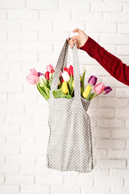 Frauenhand, die graue gepunktete Stofftasche mit bunten Tulpen hält