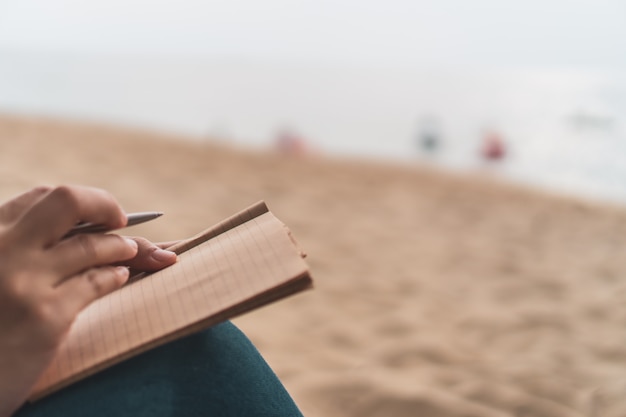 Frauenhand, die in kleines weißes Notizbuch notiert.