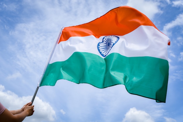 Frauenhand, die Indien-Flagge auf dem Hintergrund des blauen Himmels hält.