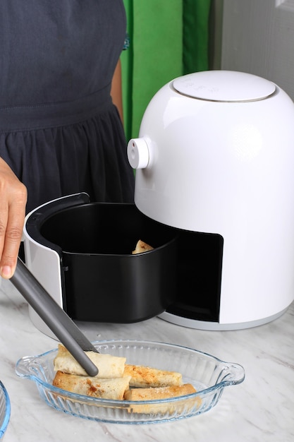 Frauenhand, die Lumpia aus der Airfryer nimmt, hausgemachte knusprige süße Lumpia mit Airfryer, gesunden Stule-Snack ohne Öl. Elektrisches Küchengerät für fettfreie Ernährung