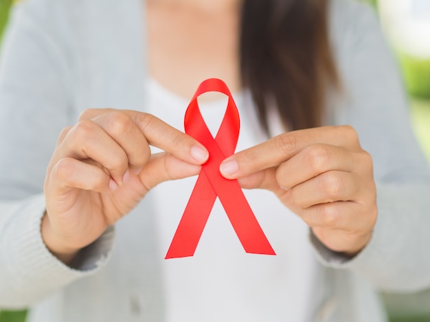 Frauenhand, die rotes Band HIV, Welt-Aids-Tagesbewusstseinsband hält