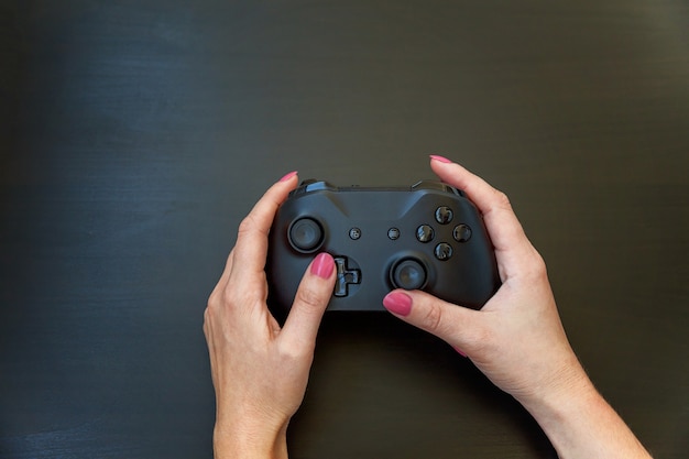 Frauenhand, die schwarzen Joystick-Gamepad hält, Spielekonsole lokalisiert auf schwarzem Hintergrund