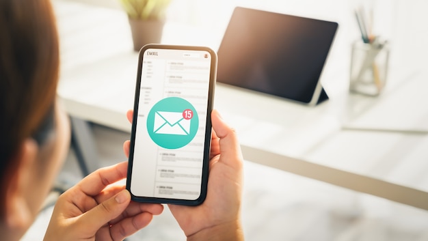 Frauenhand, die Smartphone hält und E-Mail-Bildschirm auf Anwendungsmobil im Büro zeigt.