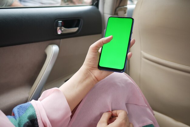 Frauenhand, die Smartphone mit grünem Bildschirm in einem Auto hält