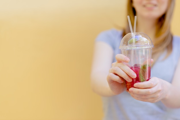 Frauenhand, die Smoothieerschütterung gegen farbige Wand hält.