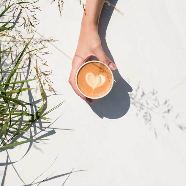 Frauenhand, die Tasse Kaffee auf einem Weiß hält.