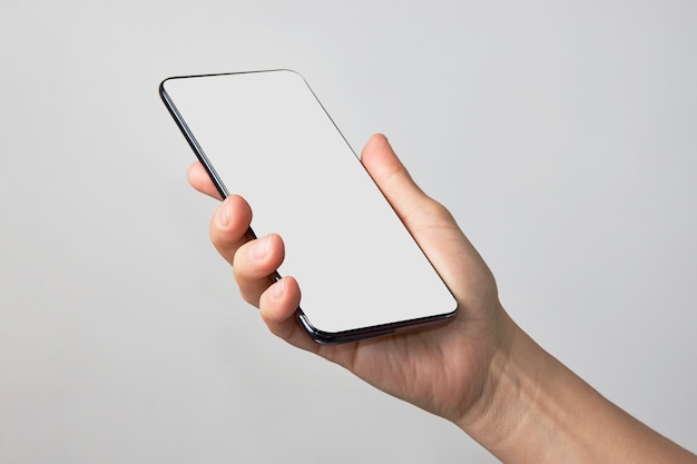 Frauenhand, die Telefon auf weißem Hintergrund mit Kopienraum hält. Frau, die Smartphone mit weißem Bildschirm hält.