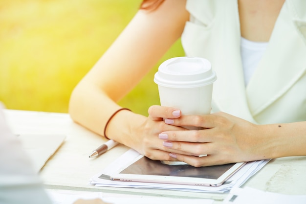 Frauenhand, die Weißbuchschale heißen Kaffee auf Tablette hält.