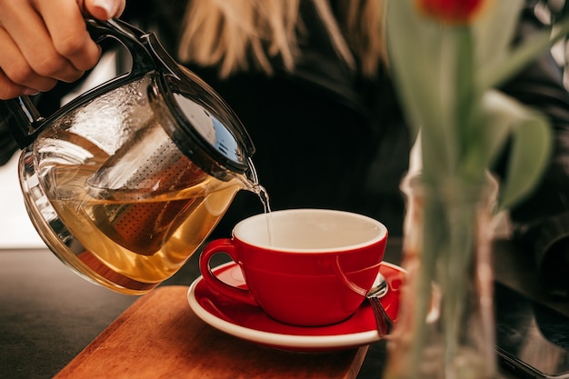 Frauenhand gießt Tee aus Glasteekanne in eine Tasse in einem Straßencafé