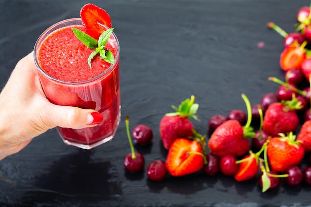 Frauenhand hält Beeren-Smoothie mit Erdbeeren und Kirschen auf schwarzem Tisch Selektiver Fokus