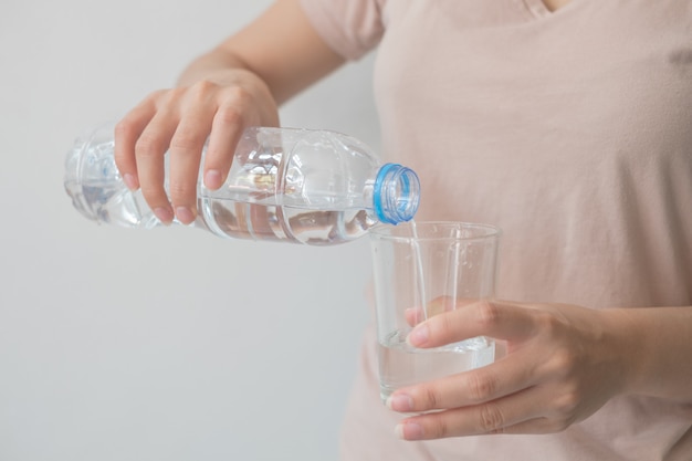 Frauenhand hält eine Flasche Wasser Wasser in ein Glas gießen