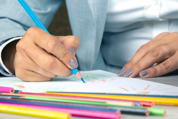 Frauenhand im Büro zeichnet mit Buntstiften auf Papier