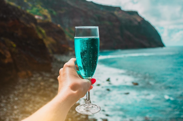 Frauenhand mit blauem Sektglas auf Ozeanhintergrundferien auf Madeira-Insel Portugal