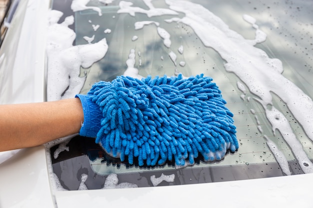 Frauenhand mit dem blauen Mikrofasergewebe, das modernes Auto des Rückspiegels wäscht oder Automobil säubert.