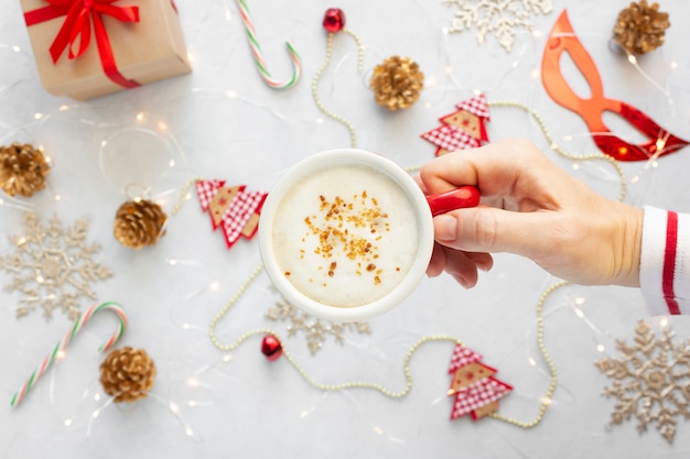 Frauenhand mit einer Tasse Cappuccino gegen Weihnachtsdekorationen