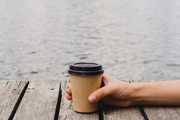 Frauenhand mit Papierkaffeetasse auf Holz