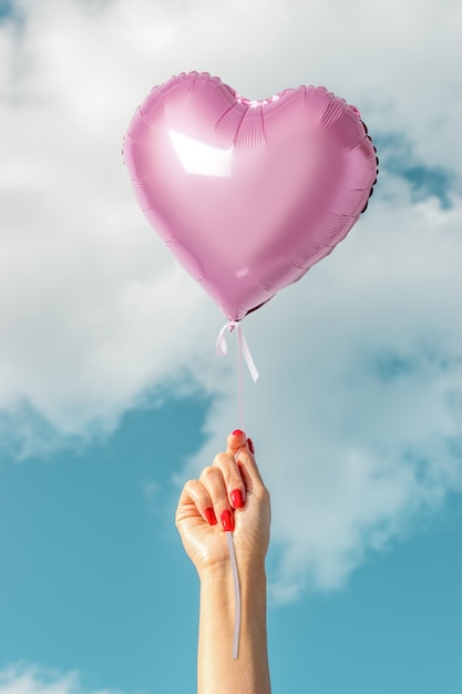 Frauenhand mit rosa Herzballon auf Himmel