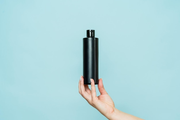 Frauenhand mit schwarzer Flasche Kosmetikprodukt zum Duschen auf blauem Hintergrund
