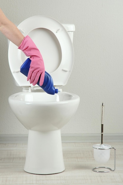Frauenhand mit Sprühflasche, die eine Toilettenschüssel in einem Badezimmer reinigt