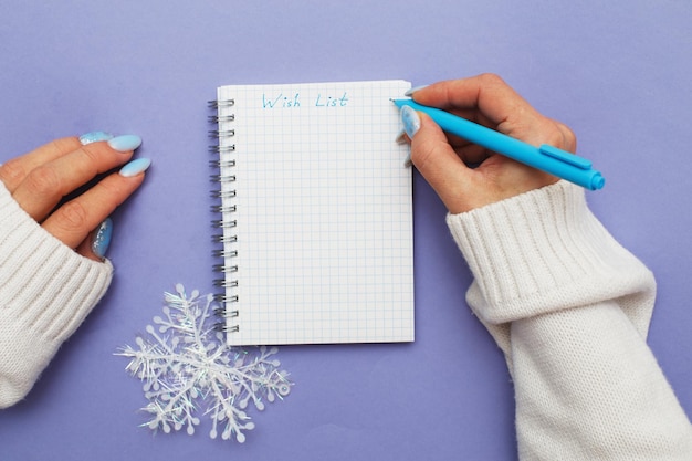 Frauenhand mit Winternägeln, die Stift auf Notizbuch halten und Wunschliste schreiben