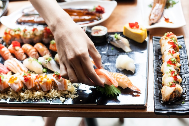 Frauenhand nehmen Sushi-Lachsfische vom Schwarzblech