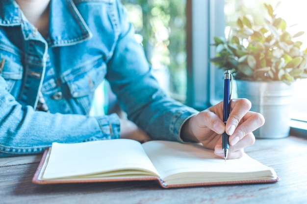 Frauenhand schreibt auf Notizbuch mit einem Stift im Büro