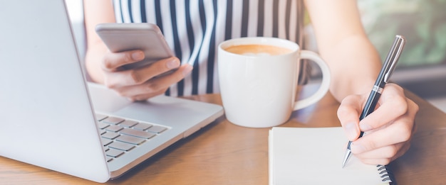 Frauenhand schreibt ein Notizbuch und benutzt ein Telefon im Büro.