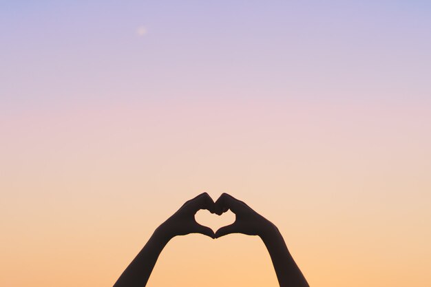 Frauenhand tun Herzform auf blauem Himmel und bokeh Hintergrund.