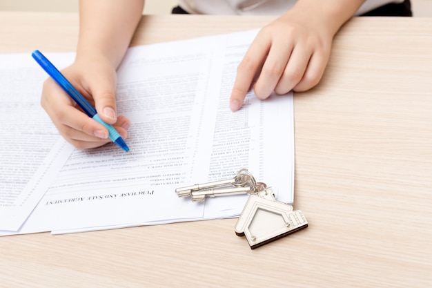 Frauenhand und Hauptschlüssel. Signierter Vertrag und Schlüssel der Immobilie mit Dokumenten.