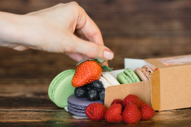 Frauenhand und Macarons mit frischen Beeren auf Holzoberfläche