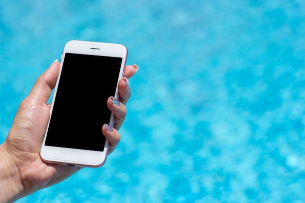 Frauenhand unter verwendung des smartphones nahe schwimmbad, nahaufnahme