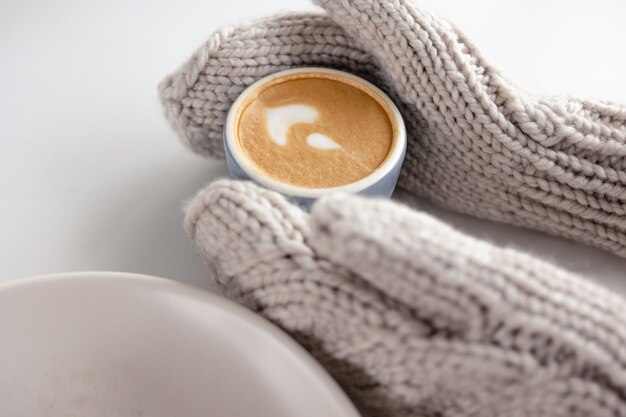 Frauenhandschuhe halten eine Kaffeetasse auf einem weißen Tisch nah oben