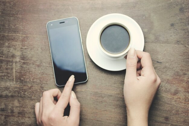 Frauenhandtelefon und Kaffee auf Holztisch