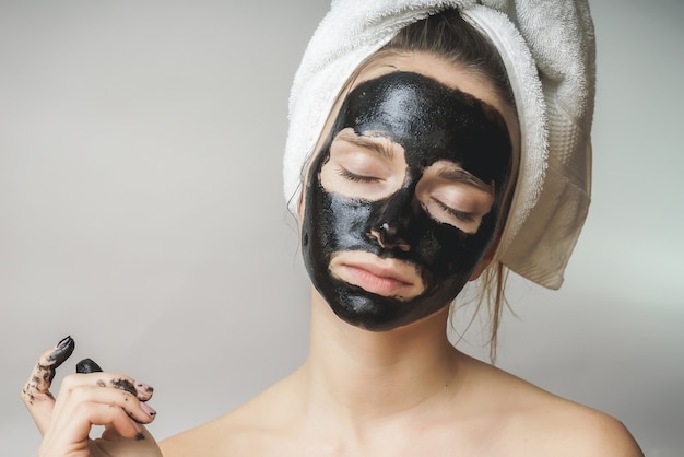 Frauenhautpflege, schwarze Maske der Kosmetik im Gesicht. Handtuch auf dem Kopf