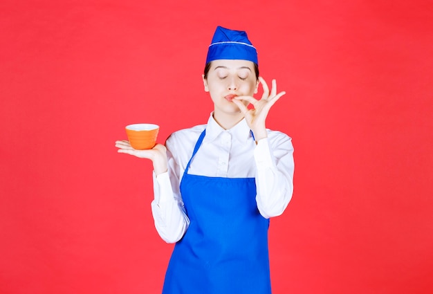 Frauenkellnerin in Uniform, die eine orangefarbene Schüssel steht und hält.