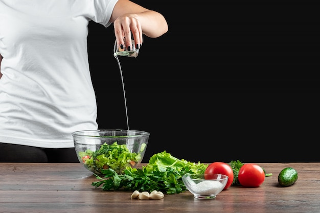 Frauenkoch fügt Olivenöl Salat hinzu und kocht Salat auf Holz.