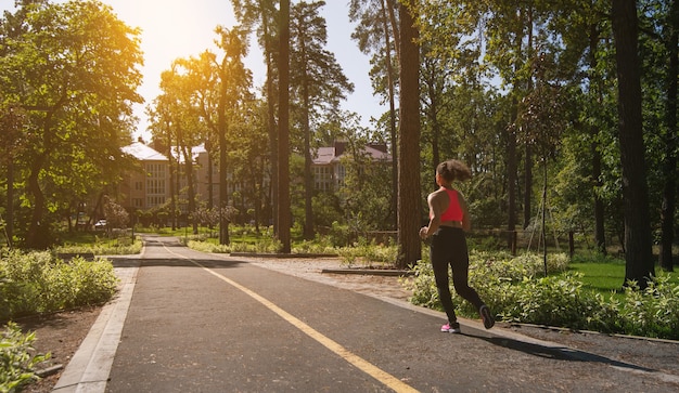 Frauenläufer, der auf einem laufenden Weg im Park joggt, der Sonnenuntergang am Ende der Straße genießt