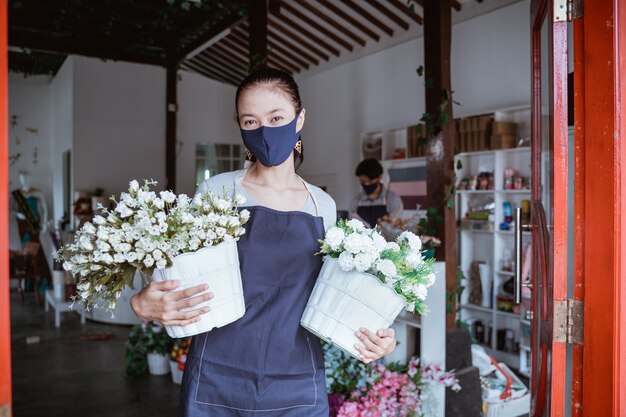 Frauenmanager, der Gesichtsmaskenflorist trägt, der Eimerblume mit ihrem Stab hält