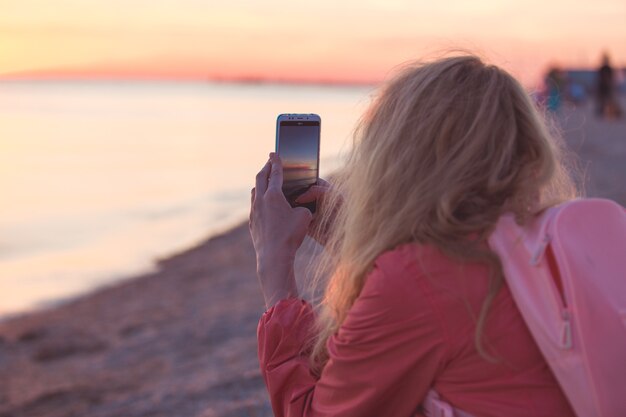 Frauenreisende, die Smartphone verwenden und den bunten Seesonnenuntergang fotografieren.